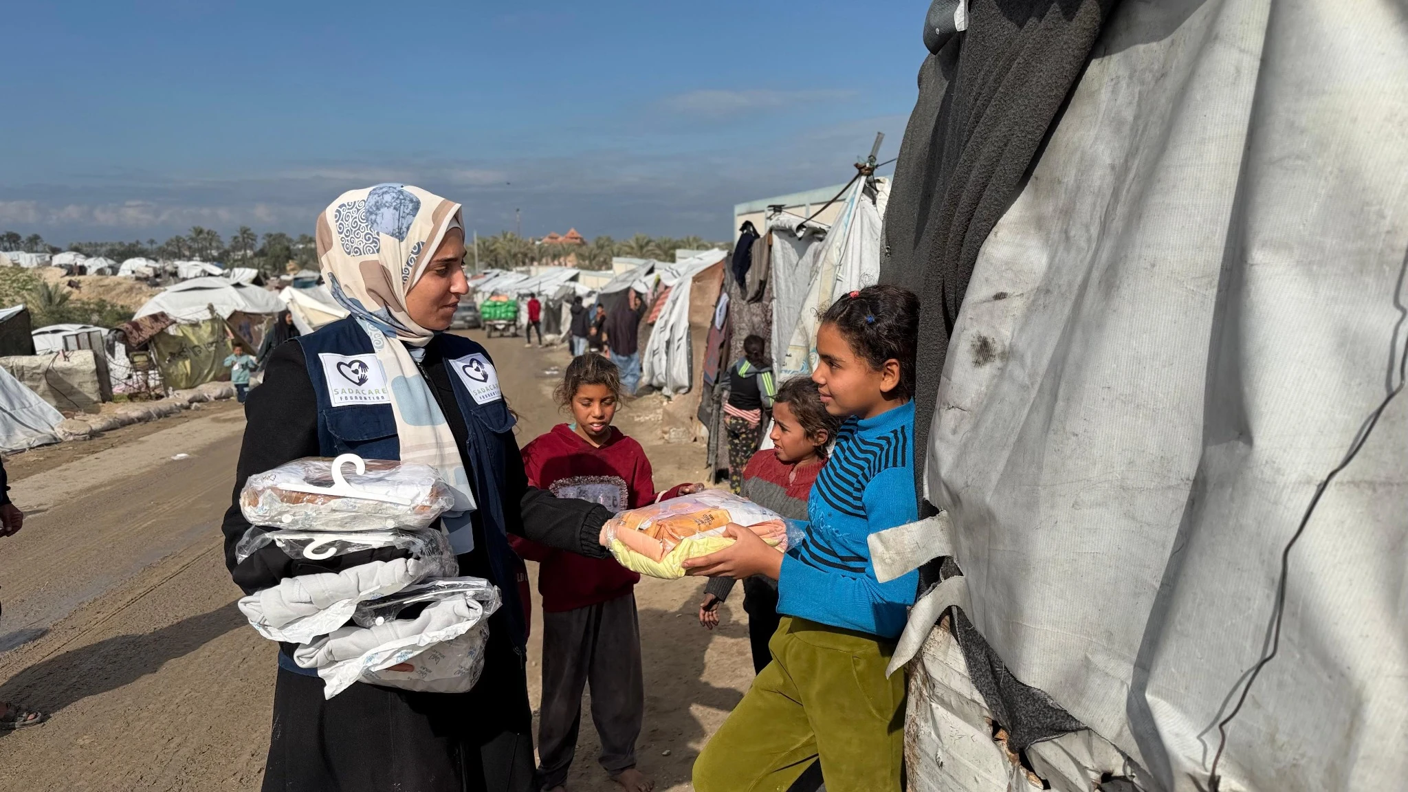 Une bénévole portant un gilet SADACARE remet des vêtements à des enfants dans un camp à Gaza